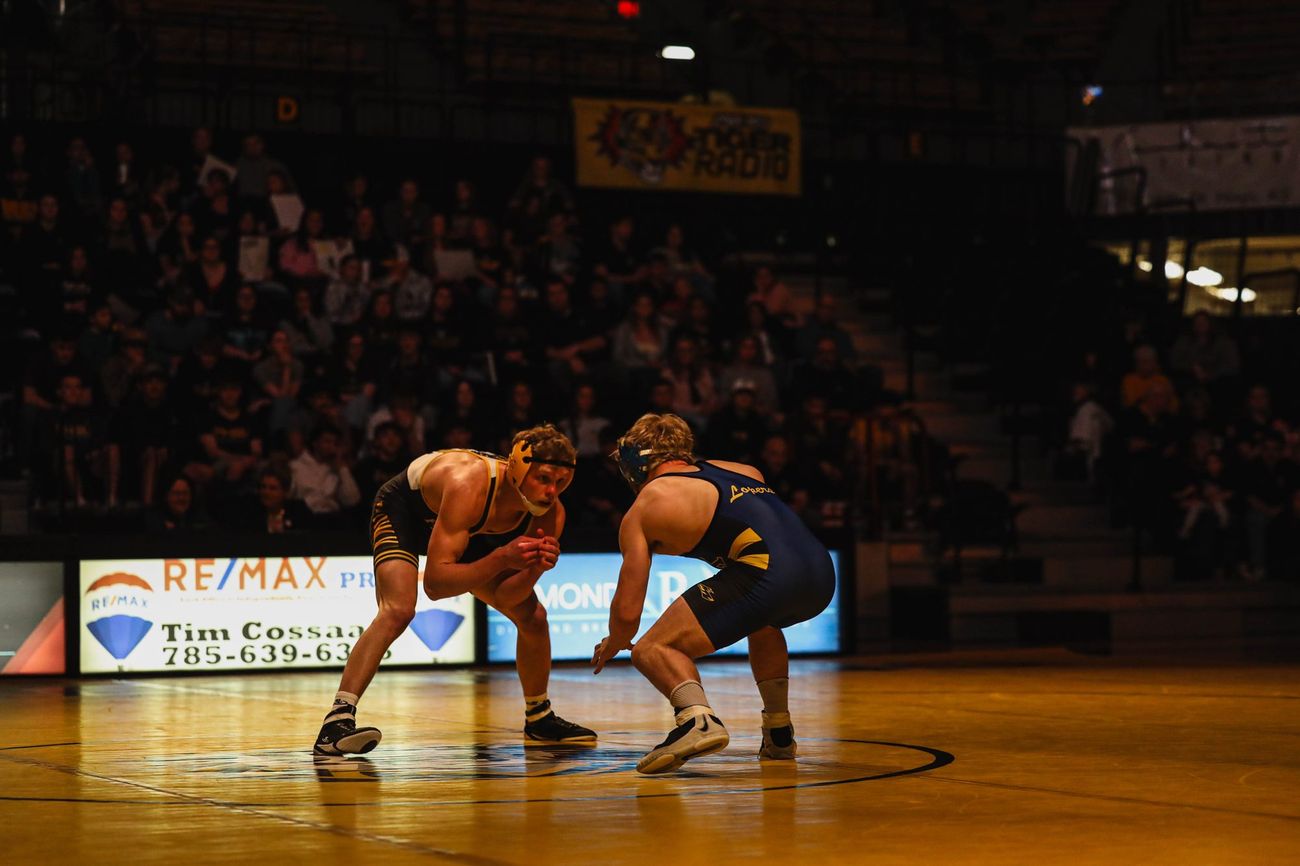 Two wrestlers squaring up at center mat in a warmly lit gym