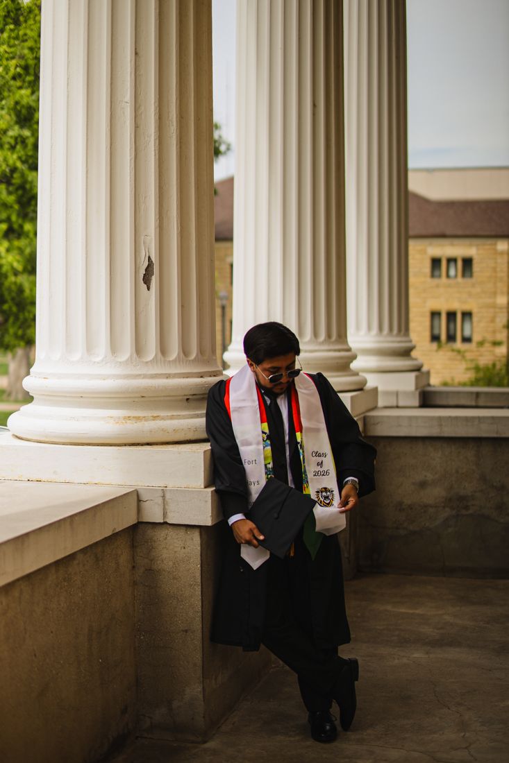 A graduate in an Honor Society stole leaning against a stone column